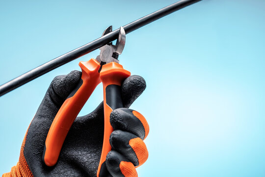 Electrician cutting wire with pliers against blue sky background. Sabotage concept.