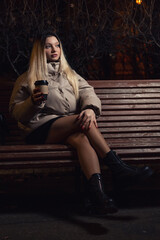 A young girl drinks coffee while sitting on a bench.