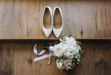 The bride's bouquet and white shoes lie on the wooden floor. Wedding photography, top view.