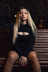 A young girl sits on a bench in the night city.