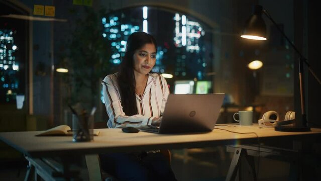 Indian Female Working in Creative Agency, Implementing Modern Business Strategy for Clients. Successful Specialist Using Laptop Computer at Night in the Office.