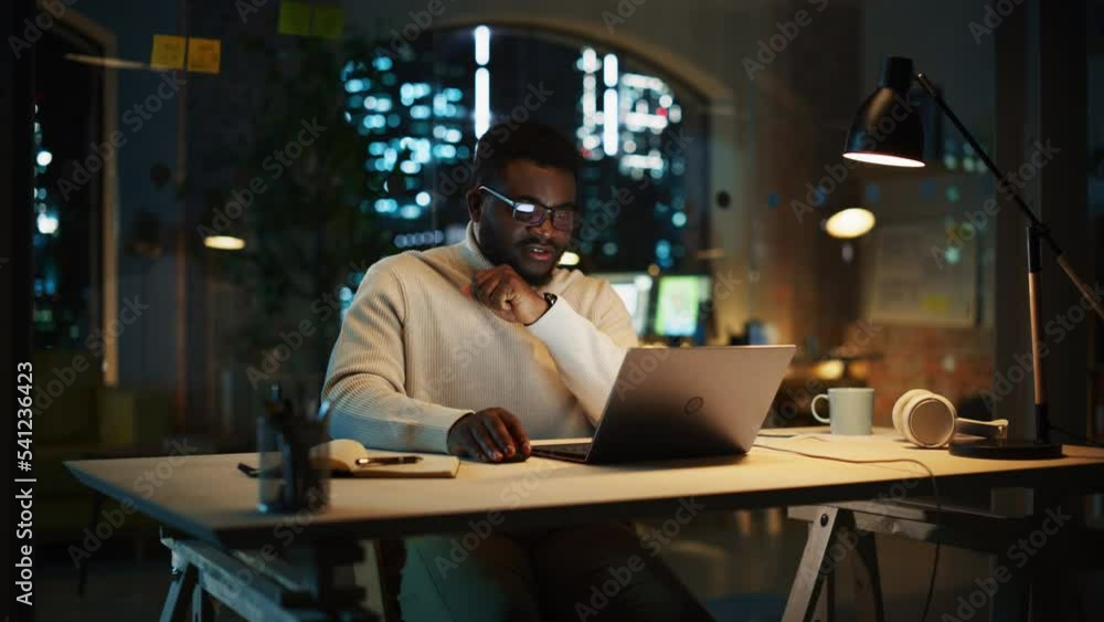 Poster creative project manager sitting at a desk, working on a laptop computer in an office at night. afri