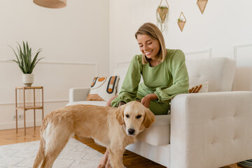 young stylish smiling woman in green summer dress petting dog at home