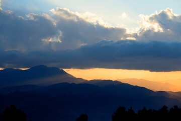 Mesmerizing soft orange sunset over the silhouette of hills with fluffy clouds in the sky