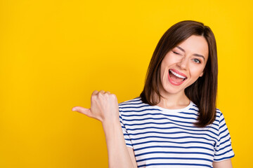 Closeup photo of young cheerful cute lady blink eye flirty directing finger empty space ad isolated on yellow color background