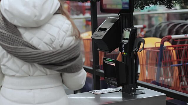 Buyer scans products through barcode scanner at self-service checkout ACO in supermarket. Assisted checkout SCO with cashless payment. Shopping at mall and store. Self-checkout
