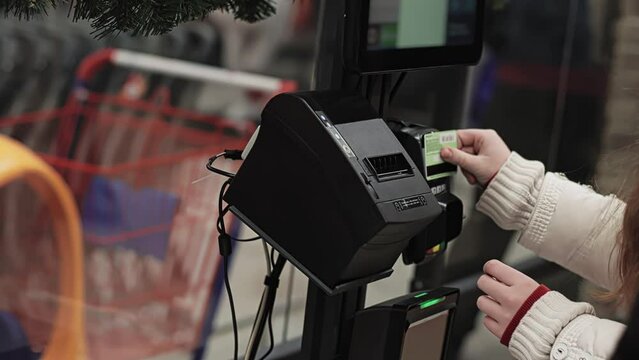 Buyer applies bank credit card to cashless payment terminal. Customer pays for purchase using plastic discount card at self-service checkout ACO. Assisted checkout SCO. Shopping at mall and store.