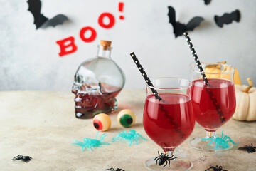 Halloween bloody cocktails. Two bloody cocktails glass goblets for Halloween and bottle form skull on light backgrounds. Decor concept for Halloween party with candy eyes, bats, spiders and pumpkins.