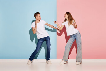 Fototapeta premium Portrait of young couple, man and woman in casual clothes dancing isolated over blue-pink background. Friendship