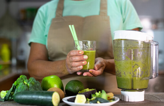 Mature Senior Woman Drinking Healthy Green Smoothie Holding A Glass With Straws. Smiling Caucasian Lady In Home Kitchen Drinking Detox Juice