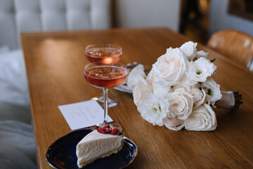 The wedding bouquet lies on the table next to the glasses and desserts.  Pink champagne in two glasses. Cheesecake in a bowl. Wedding bouquet on a wooden table.