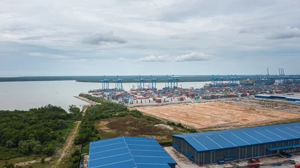 Fotobehang Klang, Malaysia - October 09, 2022: Cranes at the port Klang near Kuala Lumpur. Container crane at Klang Harbor. Aerial view on a container ship which is being loaded. Heavy Trucks at the Cargo bay © Holger