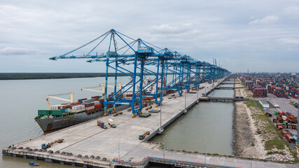 Fototapeta na wymiar Klang, Malaysia - October 09, 2022: Cranes at the port Klang near Kuala Lumpur. Container crane at Klang Harbor. Aerial view on a container ship which is being loaded. Heavy Trucks at the Cargo bay