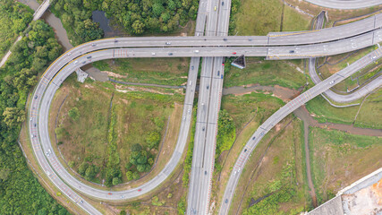 Aerial view of highway and overpass in city on a sunny day. Road traffic in city at Malaysia. Aerial view at junctions of city highway. Vehicles drive on roads. Top view of vehicles driving on street