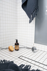 Dispenser bottle with gel and wooden brush on white tiled bathroom floor