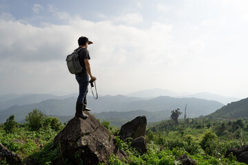 A wide shot of sian man with his backpack and camera is travel alone and look at far a way, nature travel and environment concept, copy space for individual text