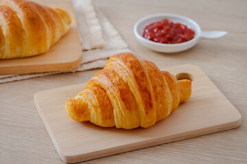 Fresh croissant on wooden board and jam on table