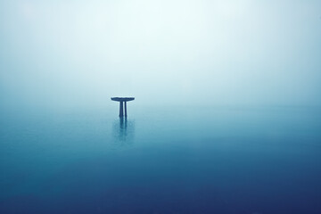 Ein alter zerfallener Brücken Pfeiler ragt im dichten See Nebel aus dem Meer.