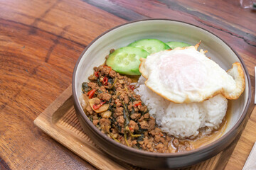 The fried meat with basil leaves and chili topped by fried egg and fresh green cucumber. 