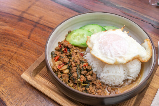 The fried meat with basil leaves and chili topped by fried egg and fresh green cucumber. 