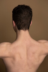 Young fit male adult stretching his shoulder, bare chest shot on a studio background