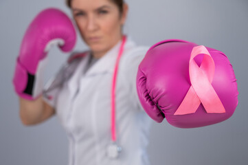 Female doctor in pink boxing gloves with a pink ribbon on a gray background. Fight against breast...