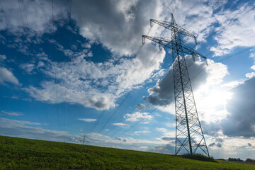 Electricity pylon for transmission and current transfer of high voltage through natural landscapes in front of cloudy sky