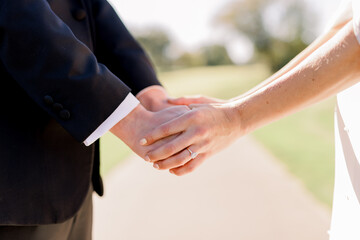 A groom wearing a suit is holding hands with a bride wearing an engagement ring