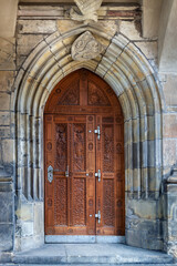 Wooden arched doors of brown color with a carved pattern on the background of a stone wall in the city of Prague. From the Doors of the World series.