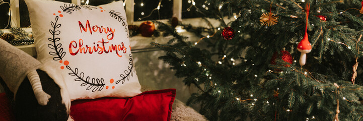 christmas and new year time. cozy soft armchair or easy chair with a comfy plaid and a red pad pillow and a gnome nisse near a decorated christmas tree. winter holiday season at home. banner