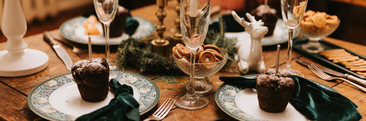 tablescapes and christmas and new year time. decorated festive kitchen cozy table with glasses, plates, cupcakes dinner food and candles. winter holiday season at home. banner