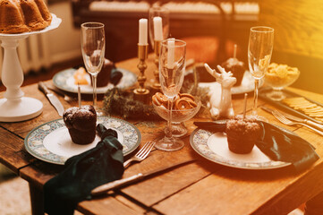 tablescapes and christmas and new year time. decorated festive kitchen cozy table with glasses, plates, cupcakes dinner food and candles. winter holiday season at home. flare