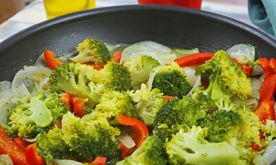Closeup of pan with steamed vegan vegetables, red paprika, green fresh broccoli, white sweet onions