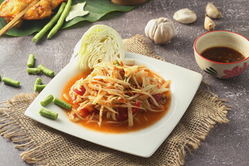 Papaya salad in a white plate served with grilled chicken and spicy dipping sauce.