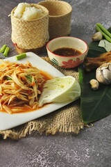 Papaya salad in a white plate served with grilled chicken and spicy dipping sauce.