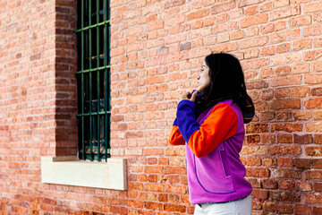 Latin brunette girl with colorful sweatshirt with orange bricks background and window