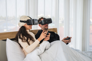 Caucasian couple wearing a VR headsets goggle device and holding game controller sitting on their...