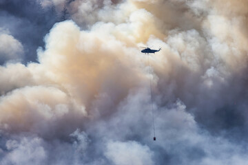 Fototapeta premium Wildfire Service Helicopter flying over BC Forest Fire and Smoke on the mountain near Hope during a hot sunny summer day. British Columbia, Canada. Natural Disaster