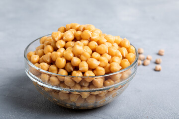 Boiled chickpeas in a glass bowl on a gray background.