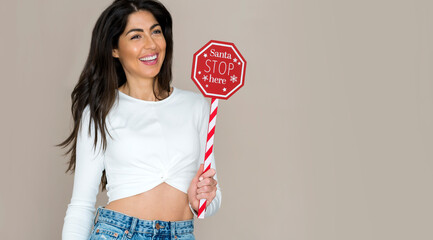 Beautiful young happy woman holding red wooden sign Santa Stop Here. Christmas shopping concept .Time for gifts