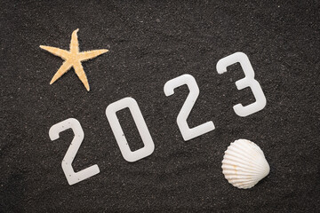 Concept de bonne année 2023 avec un coquillage et une étoile de mer sur du sable de plage noir....