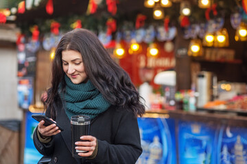 Happy woman using smart phone in city with background of festive Christmas decoration.