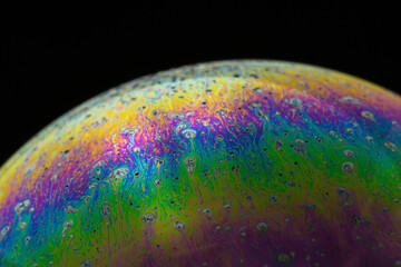 Rainbow soap bubble on a black background close-up.