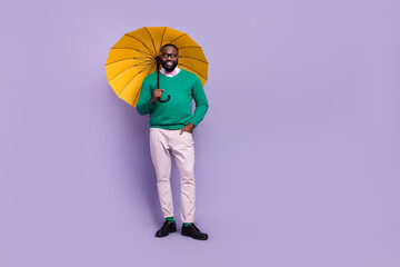Full body photo of young cheerful man go on walk during rainy weather hold yellow parasol isolated on purple color background © deagreez