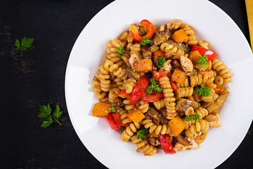 Vegetable pasta fusilli corti bucati with eggplant, sweet pepper and chicken in white plate on dark table. Top view