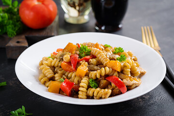 Vegetable pasta fusilli corti bucati with eggplant, sweet pepper and chicken in white plate on dark table.