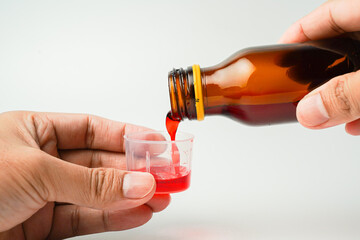 health concept, man and medicine concept - pouring medicine or antipyretic syrup from bottle into medicine cup, medicine spoon, isolated white background