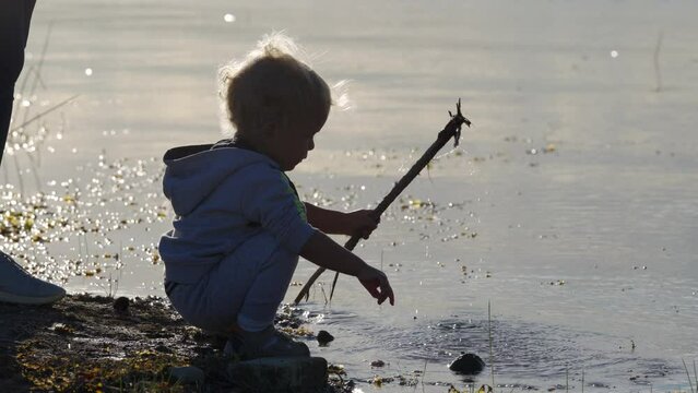 Silhouette of mother with toddler child on the shore of the lake on a summer evening at sunset. Simferopol, Crimea.