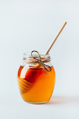 close-up on a jar of honey and a wooden spindle for honey on a white background