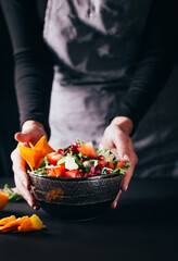 close-up on a vegetable salad in a plate that is served on the table by female hands on a dark background